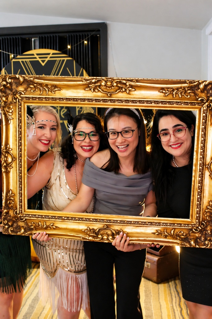 Guests smiling inside a decorative vintage gold frame during a Gatsby-themed event.