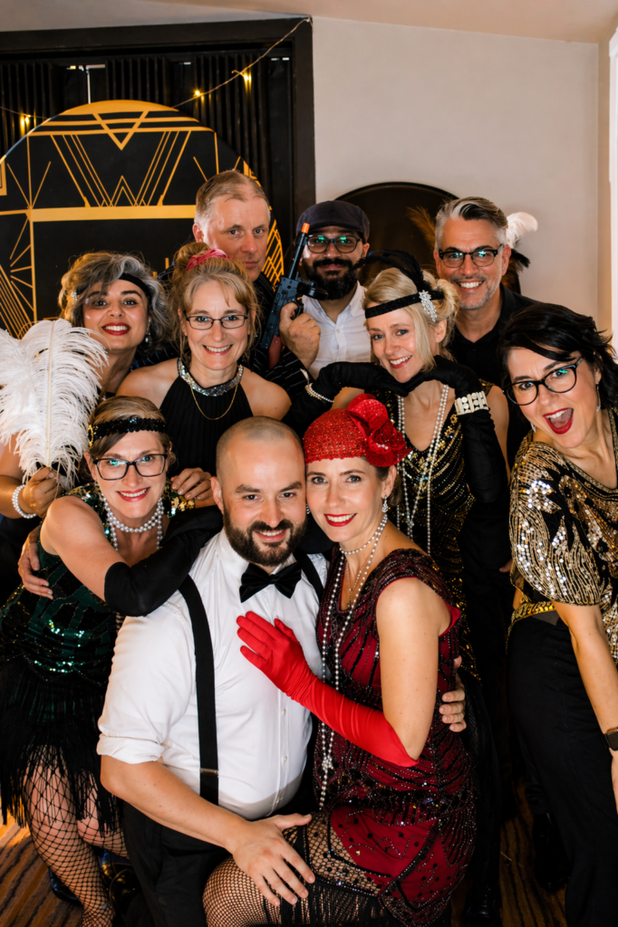 Guests dressed in 1920s-inspired outfits posing together at a Gatsby-themed event.
