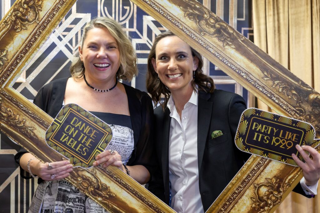 Two guests posing with Gatsby-themed signs inside a vintage gold picture frame photo booth prop.